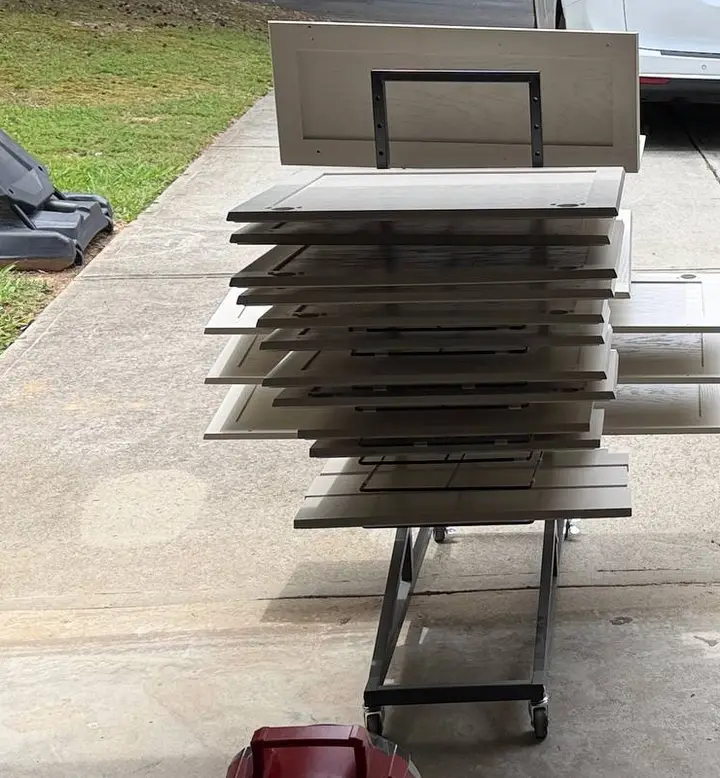 Painted cabinet doors laid flat on a rolling drying rack in a driveway