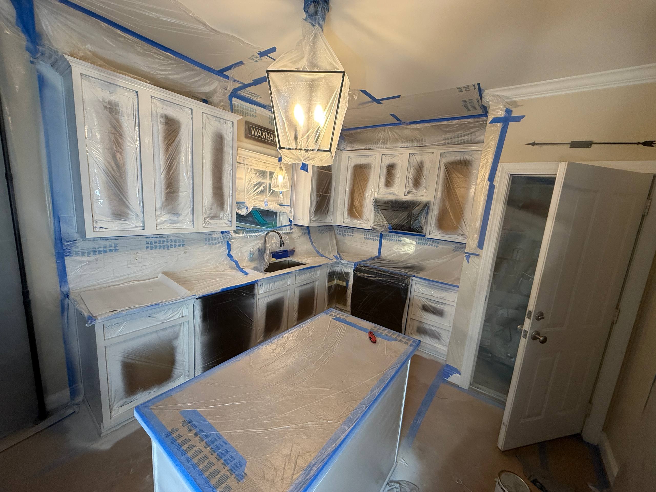 Kitchen fully masked with plastic sheeting and blue tape — containment tent protecting counters and floors