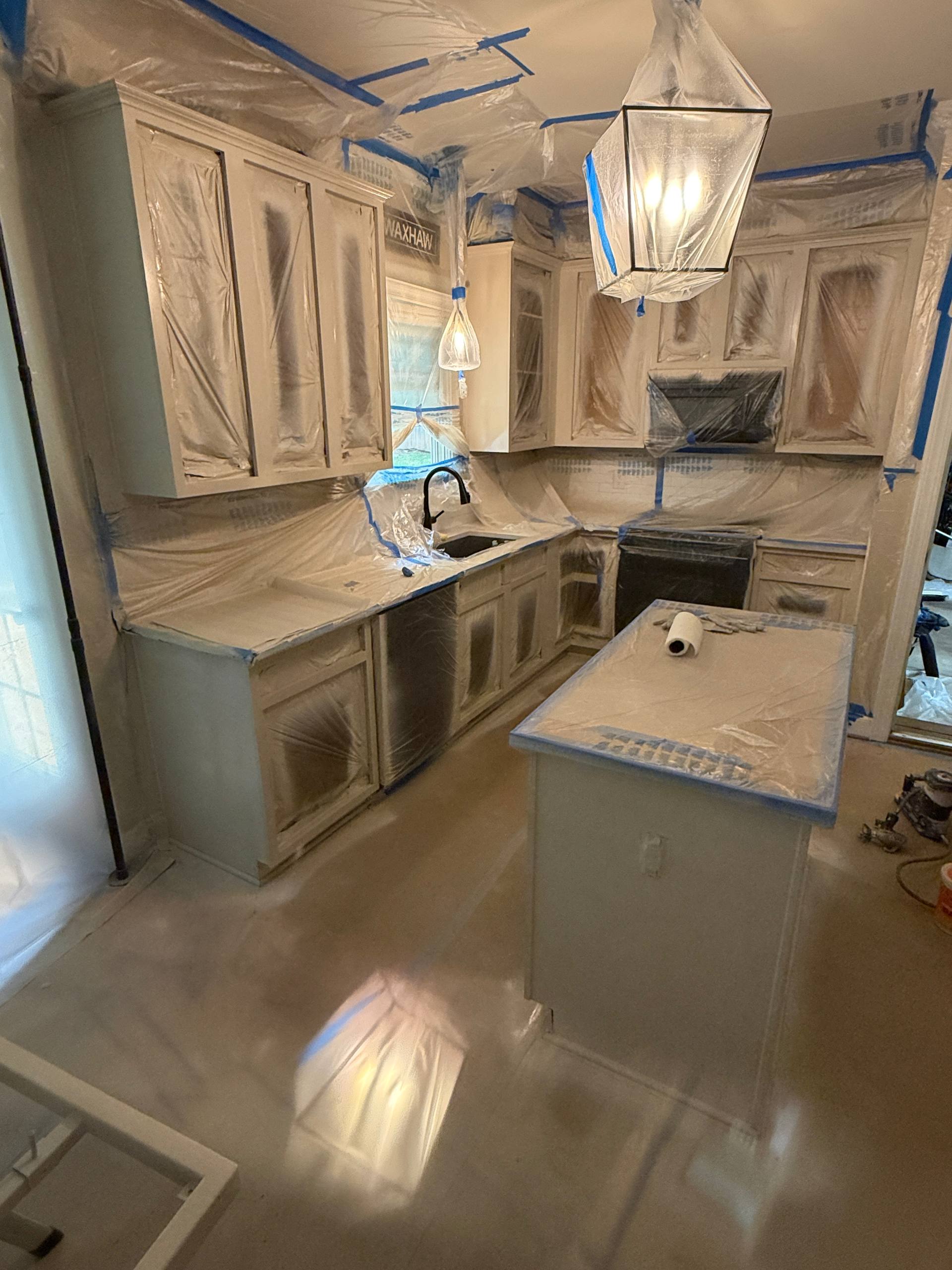 Kitchen during masking phase — full containment with blue tape, all surfaces protected before spraying